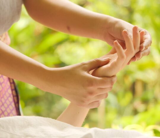Massage therapist massaging woman's hand at spa.